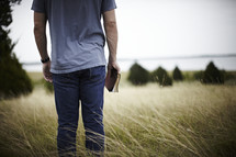 Man standing in field holding  a bible
