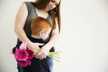 A mother hugs her young son and holds a bouquet of flowers.