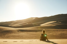 a woman sitting in a desert looking out at the view 