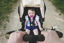 Little baby girl sitting in the pram. Hands holding stroller handle.