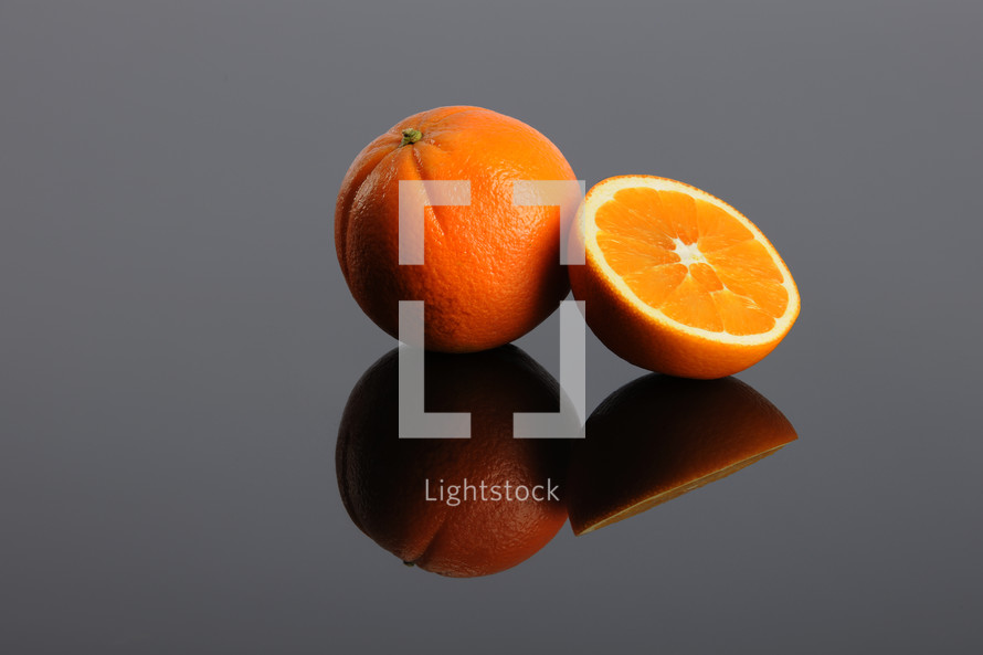 A whole orange and a sliced orange and their reflections.