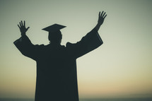 silhouette of a graduate with his hands raised 