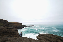 a woman sitting on cliffs along a shore 