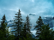 clouds over mountain peaks and evergreen trees 
