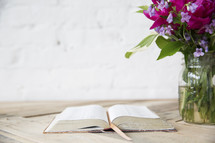 open Bible and flower in a vase on a table 