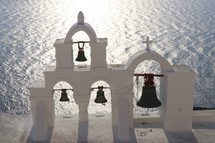 white bell tower with bells over looking the ocean 