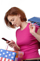 A woman carrying shopping bags and looking at her cell phone.