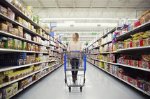 a woman pushing a shopping cart through a grocery store aisle.