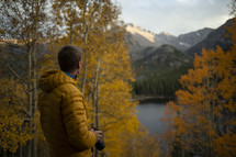man with a camera standing outdoors in fall walking towards a lake 