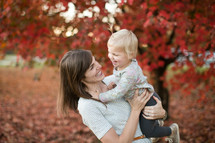 a mother holding a toddler girl outdoors in fall 