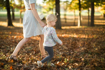mother and daughter walking through fall leaves 