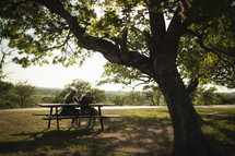 teen girls sitting at a picnic table under a tree 