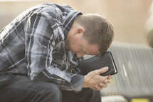 a man with his head down leaning on a Bible 