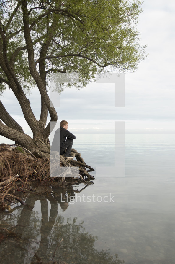 a man sitting on tree roots looking out at water