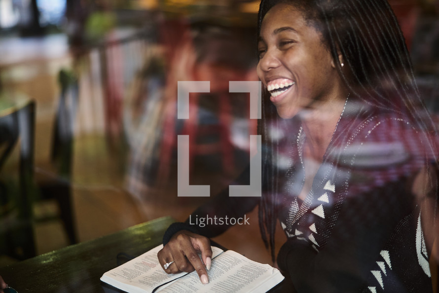 African American woman reading a Bible sitting in a coffee shop window seat