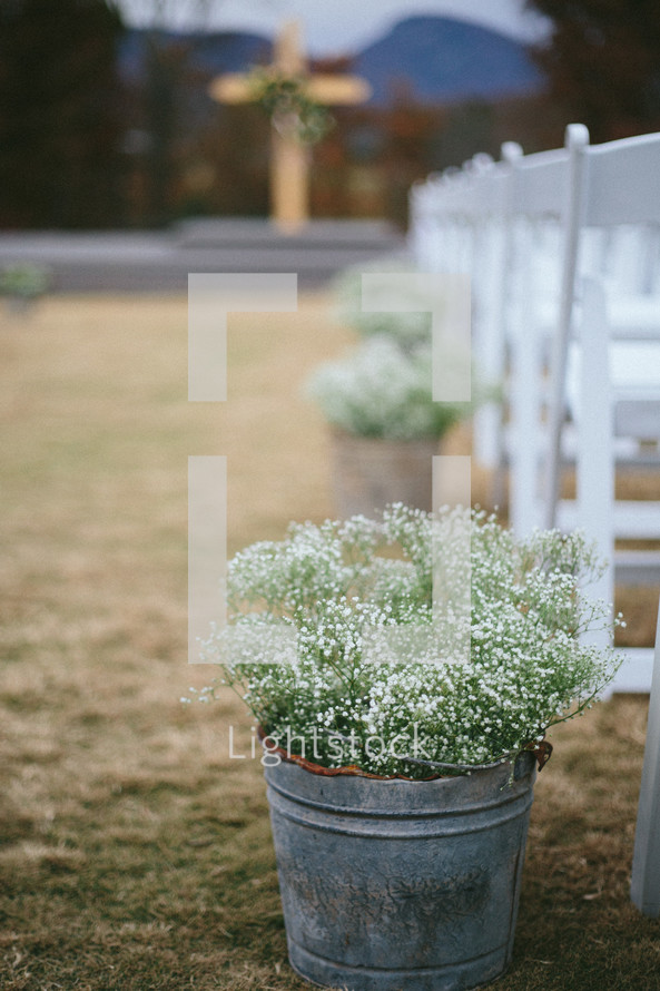 Buckets of baby's breath flowers at then end of rows of chairs, with an aisle leading to a cross.