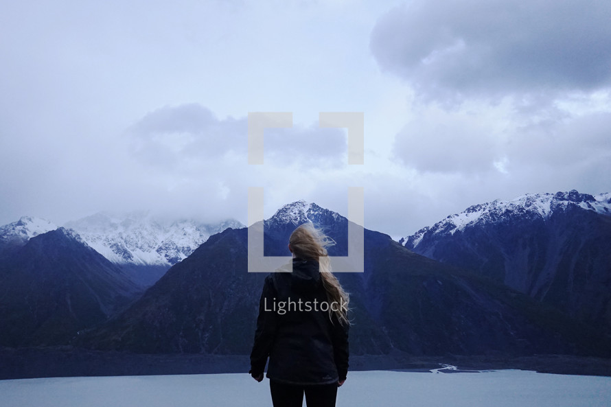 a woman in a coat looking out at mountains and lake view 