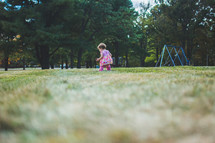 a toddler girl walking in grass on a playground 