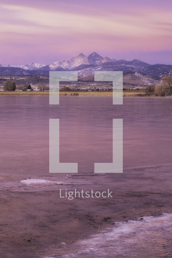 The lakes are starting to freeze over for the winter as the sunrise over Longs Peak Mountain glows in Pink in Northern Colorado