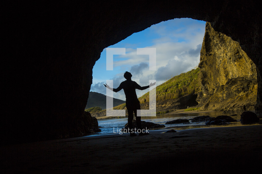 silhouette of a man with raised arms at the entrance of a cave 