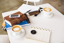 Bible, journal, notebook, coffee cup, cellphone, and pen on a white table 
