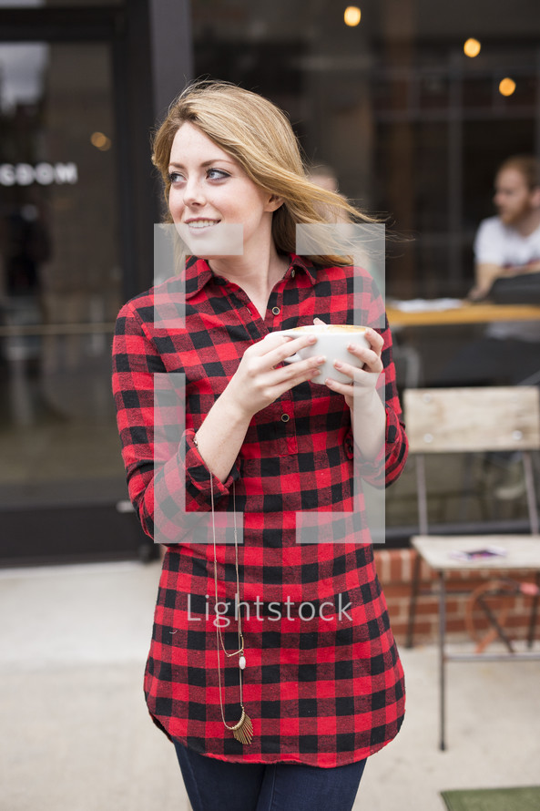 a young woman in a plaid shirt holding a coffee cup 