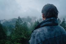 fog rising over the tops of mountains and man looking out 