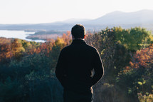 man looking out at fall trees standing on a mountain top 
