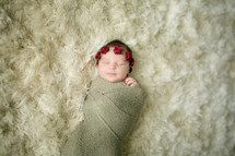 a swaddled newborn on a fur rug 