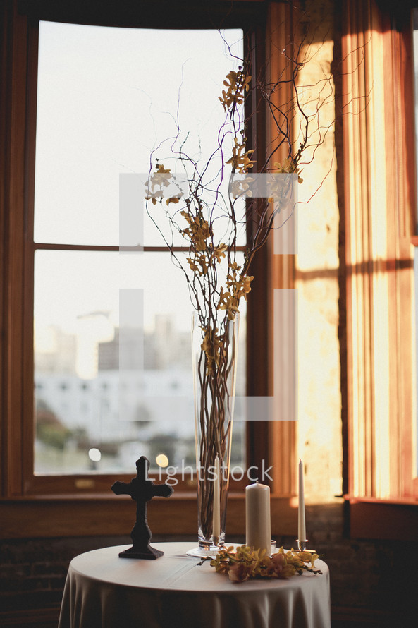 cross, vase and candles on table by a window