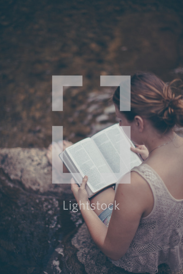 woman sitting on a rock reading a Bible 