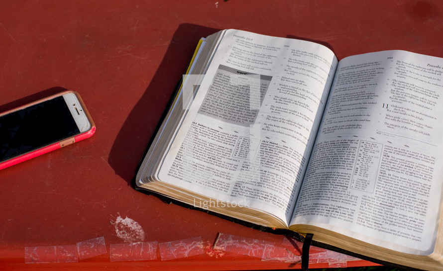 cellphone, and open Bible on a red table 