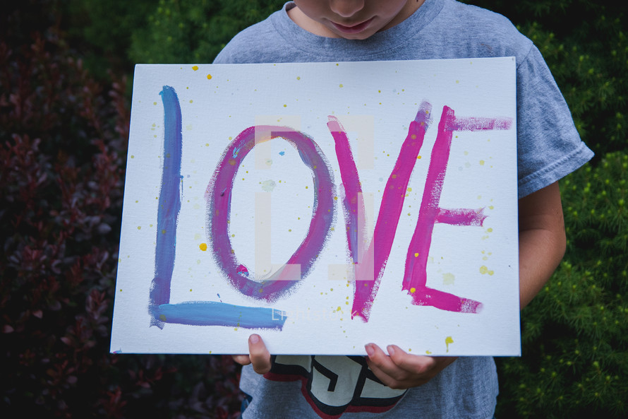 a boy holding a hand painted sign with the word love 