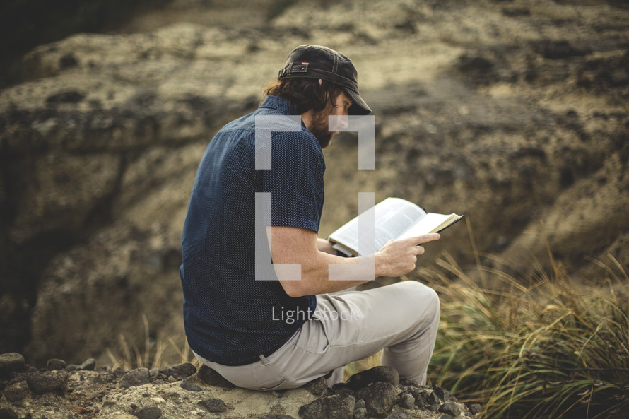 a man sitting on a rock reading a Bible 