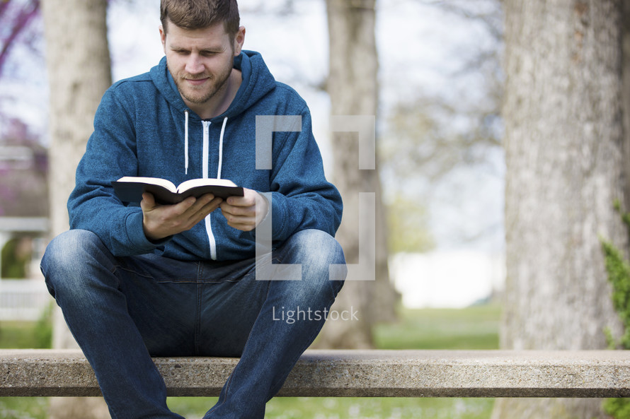 a man sitting reading a Bible outdoors 