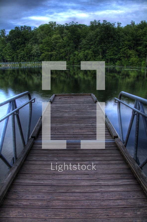 Wooden pier on the lake with reflection of the trees on the water.