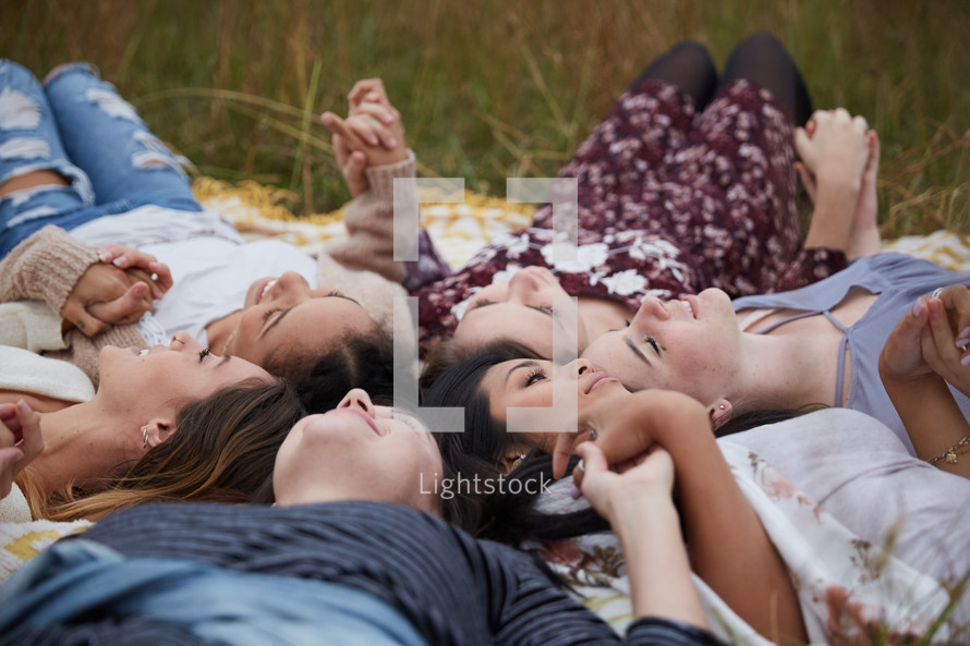 woman lying on blankets in the grass holding hands looking up 