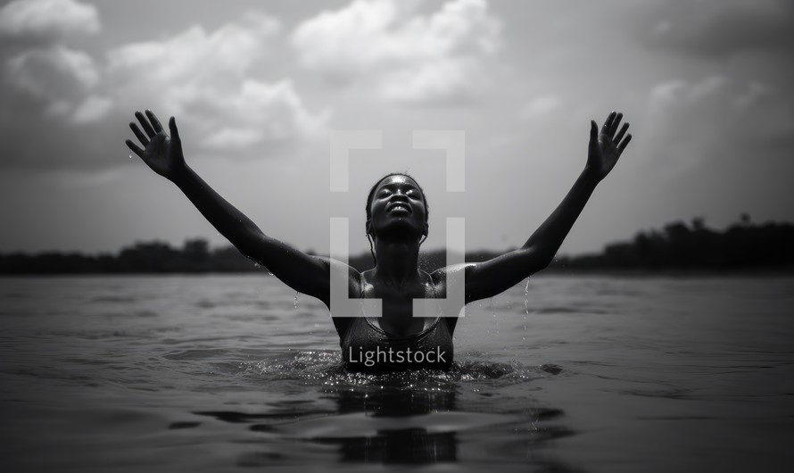 Baptism. Black and white portrait of a beautiful black woman in the water with her arms outstretched