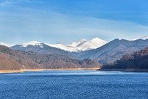 Mountain lake panorama against cloudy sky and mountains covered with snow