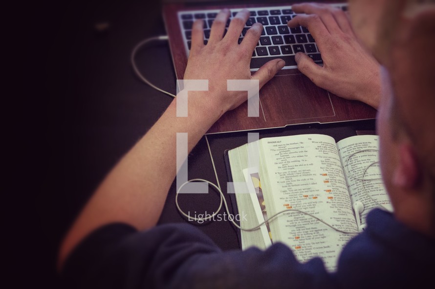 man typing on a keyboard and an open Bible 