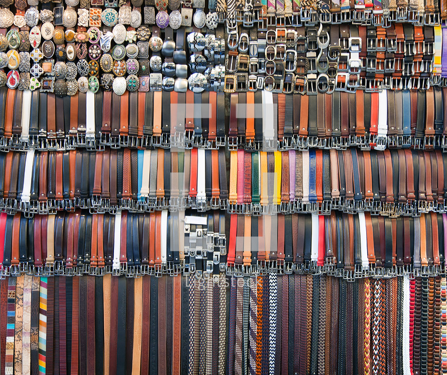 Many colored leather belts on a market.