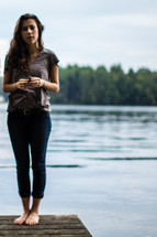 Woman standing on the corner of a wooden pier on a lake.
