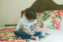 big brother holding his newborn brother on a bed 