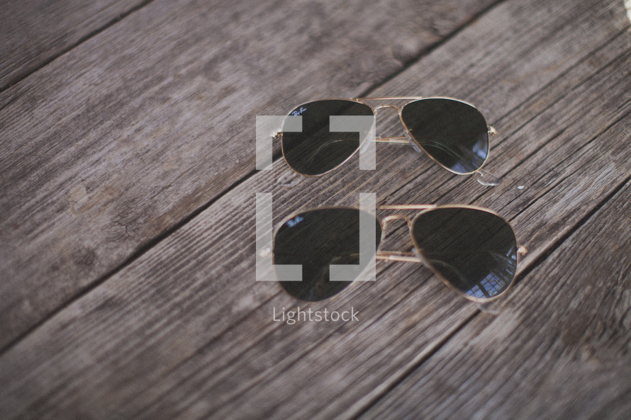 Two matching pairs of sunglasses on wood