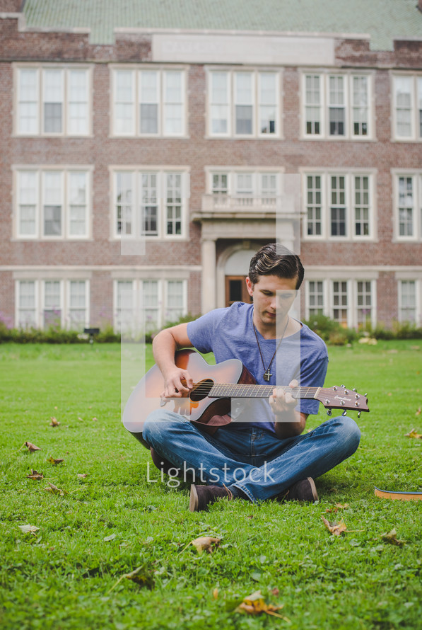 young man sitting in grass playing a guitar 