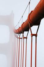 A close up of the Golden Gate Bridge suspension cables with the foggy tower in the background