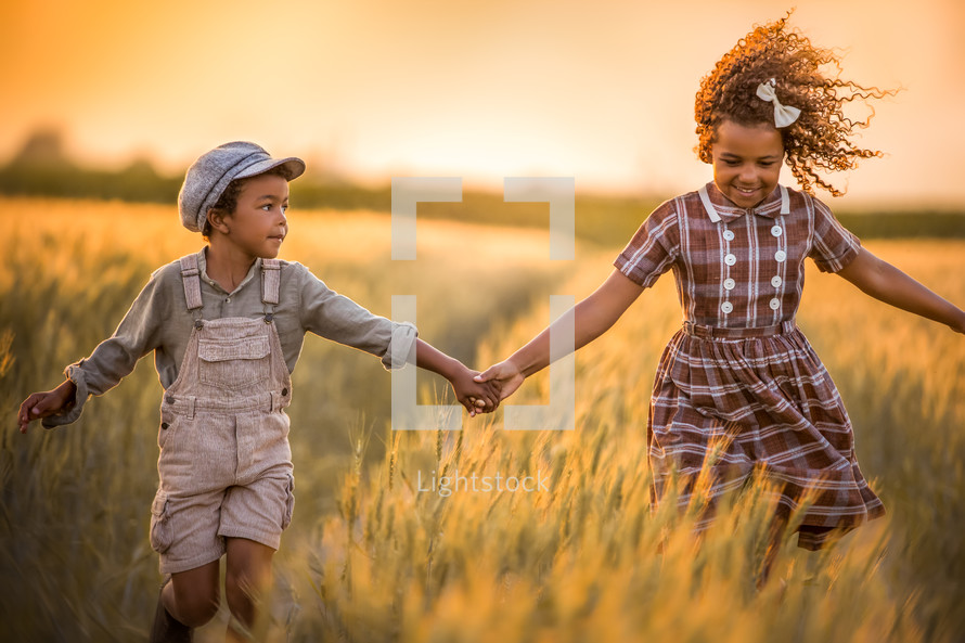 siblings running through a field holding hands 