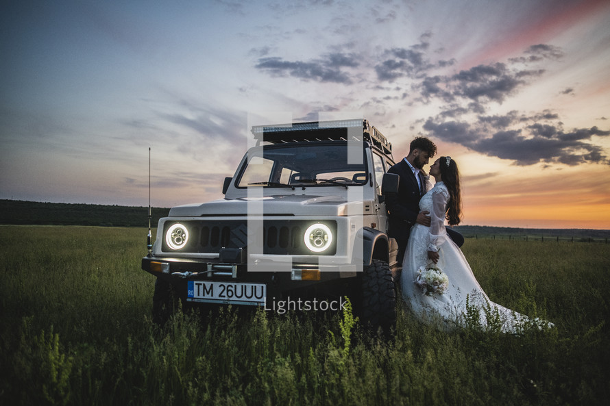 bride and groom near an SUV in a field 