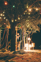 ribbons and lights hanging from a tree and blankets on the ground for a party