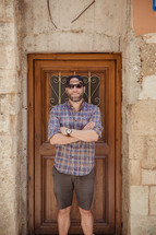 man standing with his arms crossed in front of a wood door 